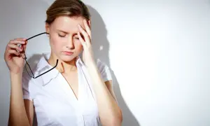 Kobieta z bólem głowy, trzymająca okulary. Czy pregabalina jest psychotropem? To pytanie nurtuje wiele osób.