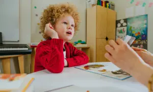 Chłopiec z kręconymi włosami, u którego zdiagnozowano orzeczenie Asperger, uczy się z kart obrazkowych.