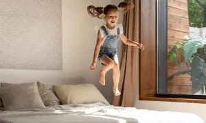 Dziewczynka w ogrodniczkach skacze na łóżku. To jej sposób na wyrażanie emocji, czyli stimming.