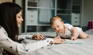 Kobieta czyta książkę dziecku leżącemu na łóżku.