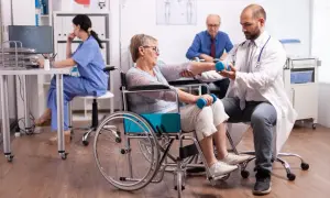 Rehabilitacja po udarze krwotocznym. Lekarz pomaga pacjentce w wózku inwalidzkim ćwiczyć z hantlami, poprawiając rokowania.
