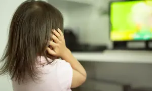 Dziewczynka z autyzmem zasłania uszy, reagując na bodźce. Ekran telewizora emituje jasne, intensywne kolory.