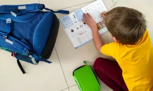 Chłopiec z autyzmem ćwiczy pisanie liter. Diagnoza funkcjonalna pomaga w nauce. Obok plecak i piórnik.