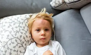 Chłopiec leży na kanapie z widocznym guzem na czole, co może sugerować wstrząs mózgu u dziecka.