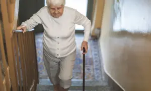 Starsza pani z laską wspina się po schodach, zmagając się z objawami parkinson w nogach.