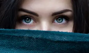 Piękne, zielone oczy, ukryte za szmaragdowym szalem. Widać tylko górną część twarzy, sugerującą unikanie kontaktu wzrokowego.