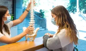 Fizjoterapeuta wyjaśnia pacjentce model kręgosłupa, omawiając, czy z przepukliną kręgosłupa można pracować.