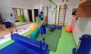 Sala do terapii integracji sensorycznej: huśtawki, drabinki, piłki i materace do ćwiczeń.