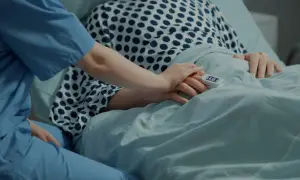 Pielęgniarka trzyma dłoń pacjenta w stanie minimalnej świadomości, rokowania niepewne. Pulsoksymetr na palcu.