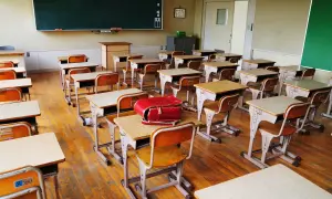 Pusta klasa z rzędami ławek i krzeseł, gotowa na lekcje w szkole dla dzieci z autyzmem. Czerwony tornister leży na jednej z ławek.