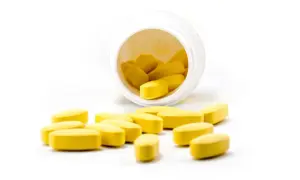 Żółte tabletki rozsypane z białego pojemnika. Czy propranolol uspokaja? To pytanie nurtuje wiele osób szukających ulgi.