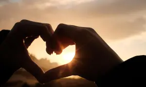 Dłonie tworzą serce na tle zachodzącego słońca. Początek pięknej historii, która może być jak love bombing.