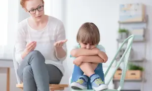 Zestresowany chłopiec z autyzmem, który uderza głową, siedzi skulony, podczas gdy terapeuta próbuje go uspokoić.