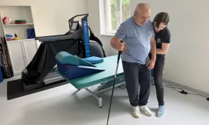 Rehabilitacja po udarze niedokrwiennym. Pacjent z pomocą fizjoterapeuty ćwiczy chód z laską. Rokowania są dobre.