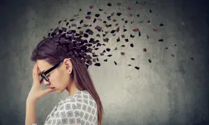 Kobieta z ręką na czole, której głowa rozpada się na fragmenty. Obraz symbolizuje **adhd z przewagą zaburzeń koncentracji uwagi**, trudności w skupieniu myśli.