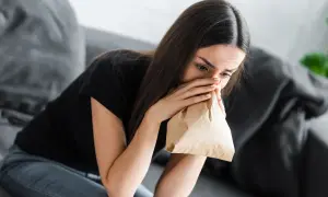 Kobieta z papierową torbą przy ustach, doświadczająca objawów hiperwentylacji.
