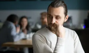 Mężczyzna zamyślony, jak osoba wysoko wrażliwa, czuje się przytłoczony hałasem i rozmowami w tle.