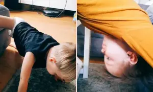 Dziecko w czarnej koszulce na podłodze, z głową pochyloną do przodu. Obok, pod pomarańczową tkaniną, widać twarz dziecka. To autystyczne machanie rączkami.
