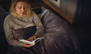 Kobieta z nadwrażliwością sensoryczną u dorosłych, otulona kocem, czyta książkę w przytulnym wnętrzu.