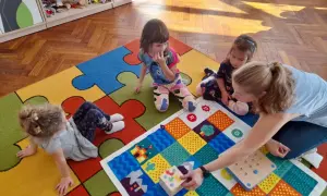 Wspólna zabawa w przedszkolu, gdzie dzieci z autyzmem uczą się przez interakcję. Kolorowa mata i pomoce dydaktyczne wspierają rozwój.