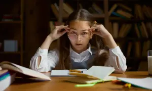 Dziewczynka w okularach, z rękami przy skroniach, skupiona na nauce. Widać jej zaangażowanie i funkcje uwagi podczas studiowania.