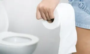 Dłoń trzymająca rolkę papieru toaletowego, w tle toaleta. Stres wywołuje biegunka.
