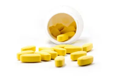 Żółte tabletki rozsypane z białego pojemnika. Czy propranolol uspokaja? To pytanie nurtuje wiele osób szukających ulgi.