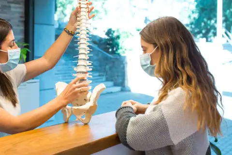 Fizjoterapeuta wyjaśnia pacjentce model kręgosłupa, omawiając, czy z przepukliną kręgosłupa można pracować.