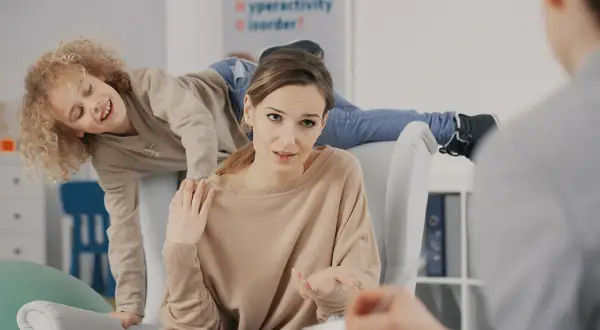 Matka rozmawia z terapeutą o różnych rodzajach ADHD, podczas gdy jej syn z nadpobudliwością bawi się za jej plecami.