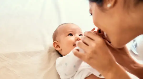 Mama czule całuje swoje dziecko, które wpatruje się w nią z zaciekawieniem. Może to być sygnał, że dziecko nie reaguje na imię, ale miłość mamy jest dla niego najważniejsza.