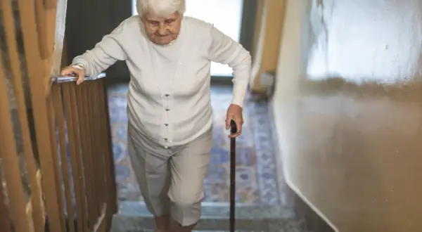 Starsza pani z laską wspina się po schodach, zmagając się z objawami parkinson w nogach.