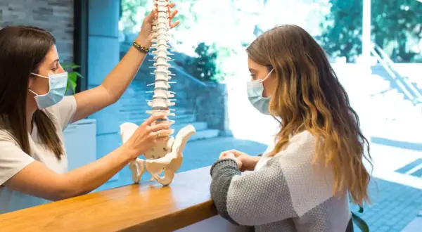 Fizjoterapeuta wyjaśnia pacjentce model kręgosłupa, omawiając, czy z przepukliną kręgosłupa można pracować.