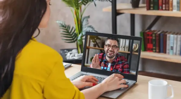 Kobieta na wideo rozmowie z mężczyzną, który uśmiecha się i macha. Może to być konsultacja online, np. test na aspergera.