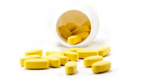 Żółte tabletki rozsypane z białego pojemnika. Czy propranolol uspokaja? To pytanie nurtuje wiele osób szukających ulgi.
