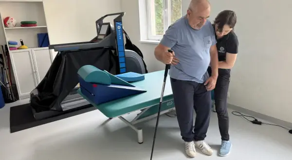 Rehabilitacja po udarze niedokrwiennym. Pacjent z pomocą fizjoterapeuty ćwiczy chód z laską. Rokowania są dobre.