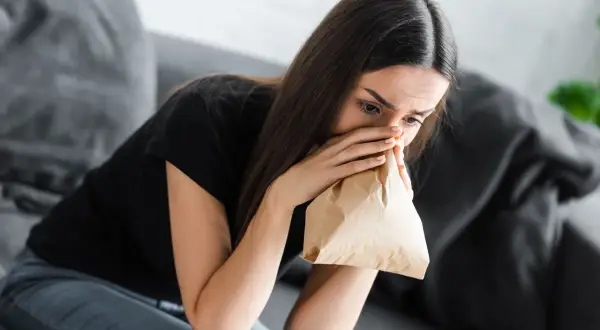 Kobieta z papierową torbą przy ustach, doświadczająca objawów hiperwentylacji.