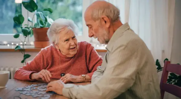 Para seniorów układa puzzle, ciesząc się wspólnymi ćwiczeniami umysłowymi.