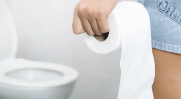 Dłoń trzymająca rolkę papieru toaletowego, w tle toaleta. Stres wywołuje biegunka.