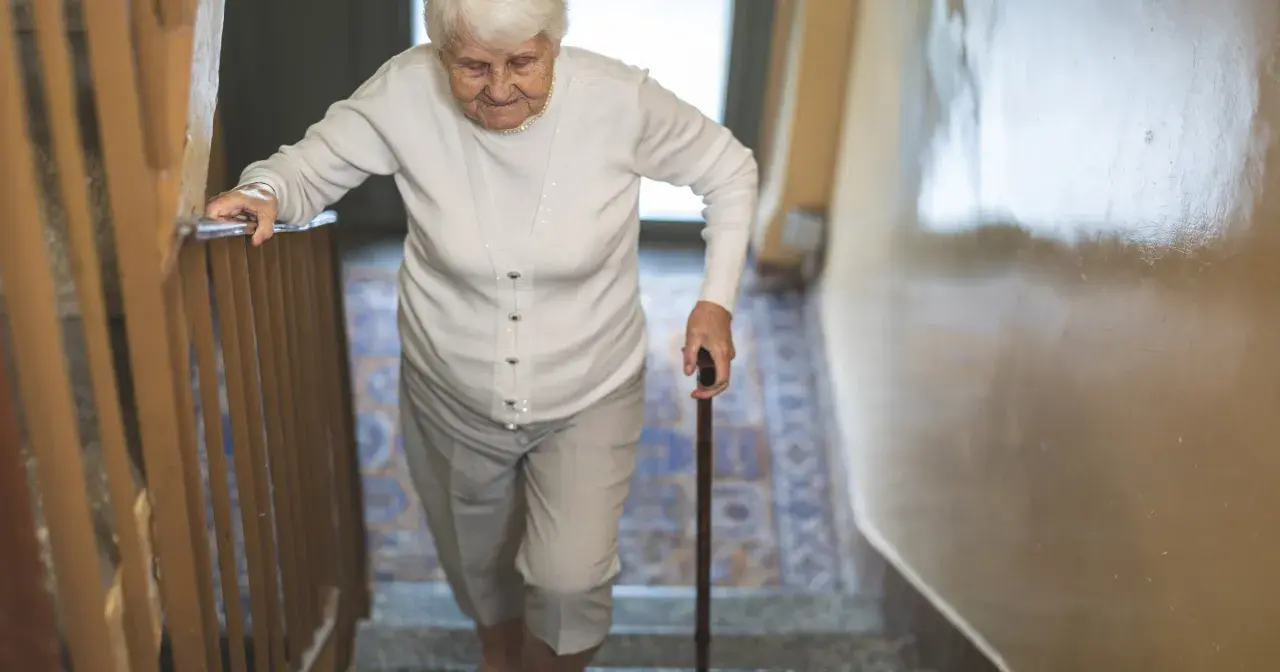 Starsza pani z laską wspina się po schodach, zmagając się z objawami parkinson w nogach.