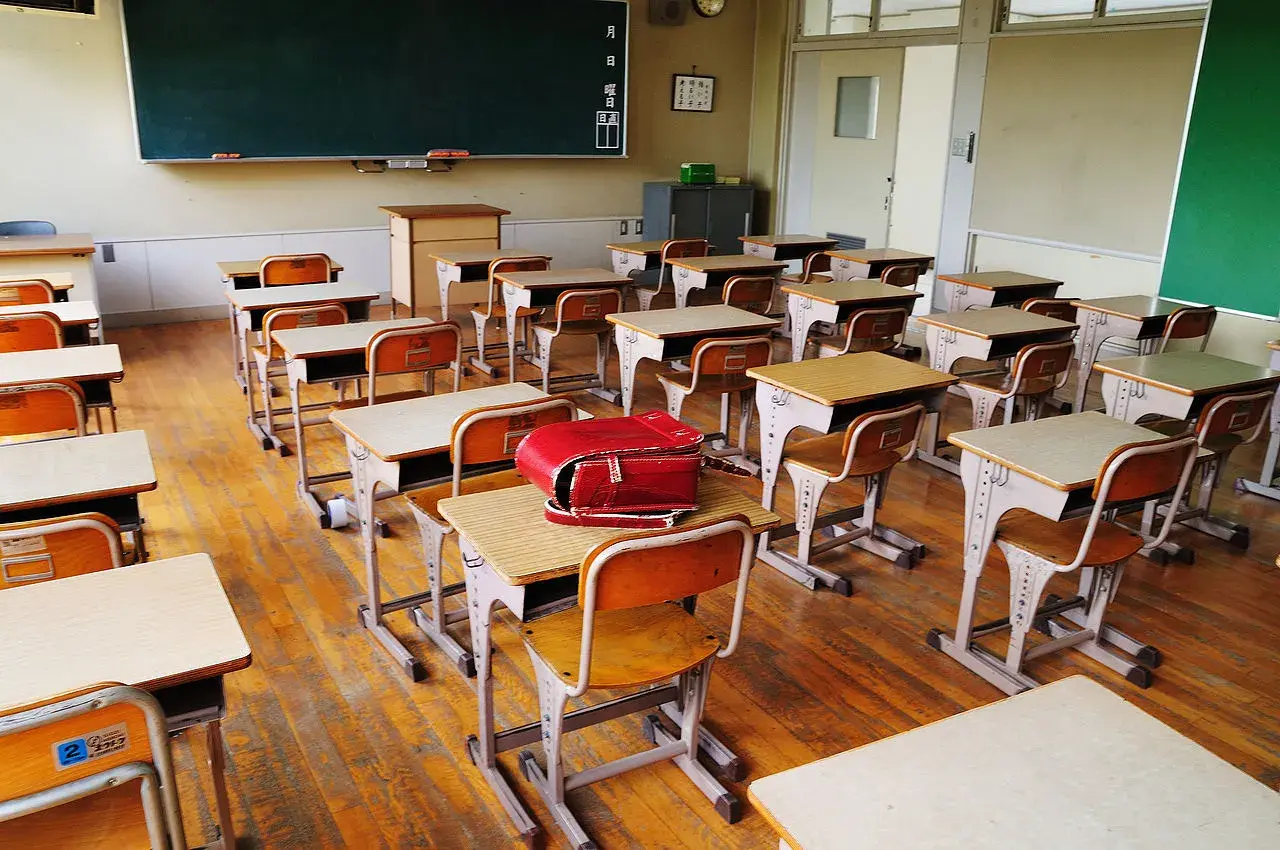Pusta klasa z rzędami ławek i krzeseł, gotowa na lekcje w szkole dla dzieci z autyzmem. Czerwony tornister leży na jednej z ławek.