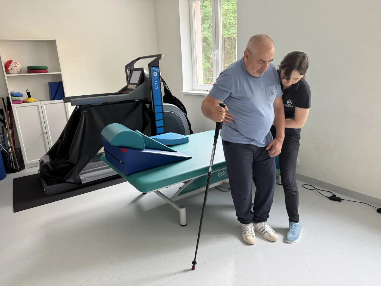Rehabilitacja po udarze niedokrwiennym. Pacjent z pomocą fizjoterapeuty ćwiczy chód z laską. Rokowania są dobre.