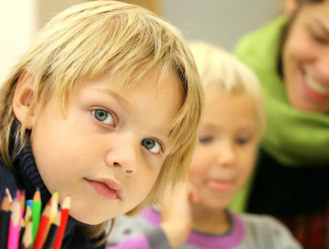 Chłopiec z niebieskimi oczami i blond włosami, obok niego inne dziecko i uśmiechnięta osoba. Jak uspokoić dziecko z Aspergerem?