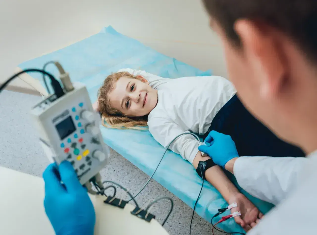 Uśmiechnięta dziewczynka leży na łóżku podczas badania EEG, które pomaga diagnozować padaczkę u dzieci.