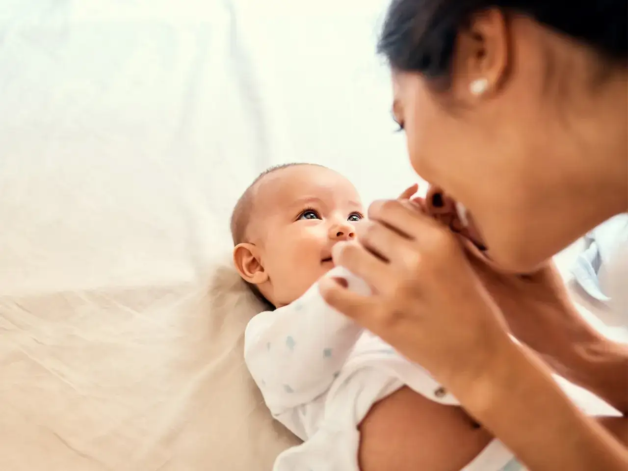 Mama czule całuje niemowlę, które wpatruje się w nią z zaciekawieniem. Dziecko nie reaguje na imię, ale jego oczy błyszczą radością.