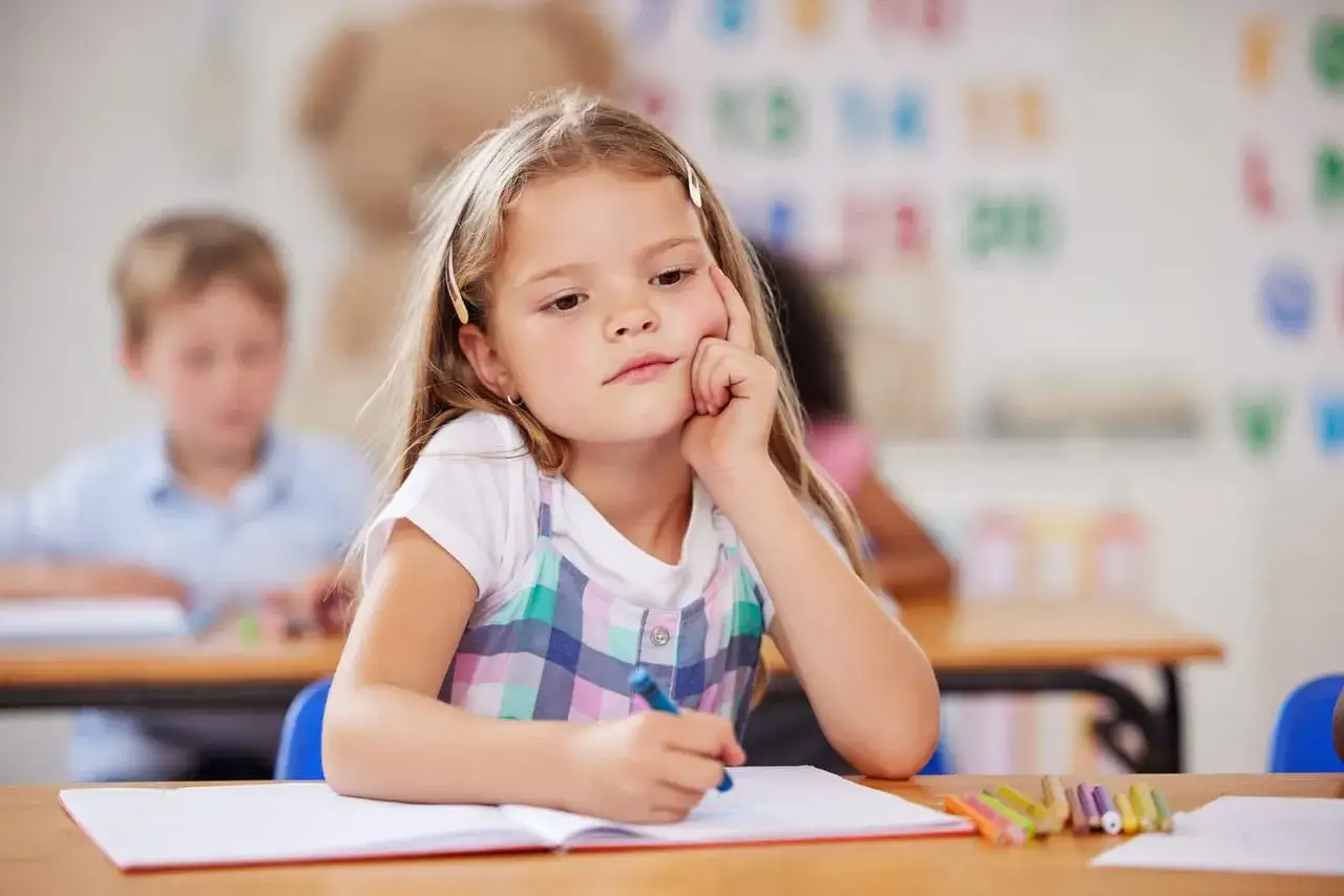 Dziewczynka z ADHD, zamyślona, opiera głowę na dłoni, rysując niechętnie.