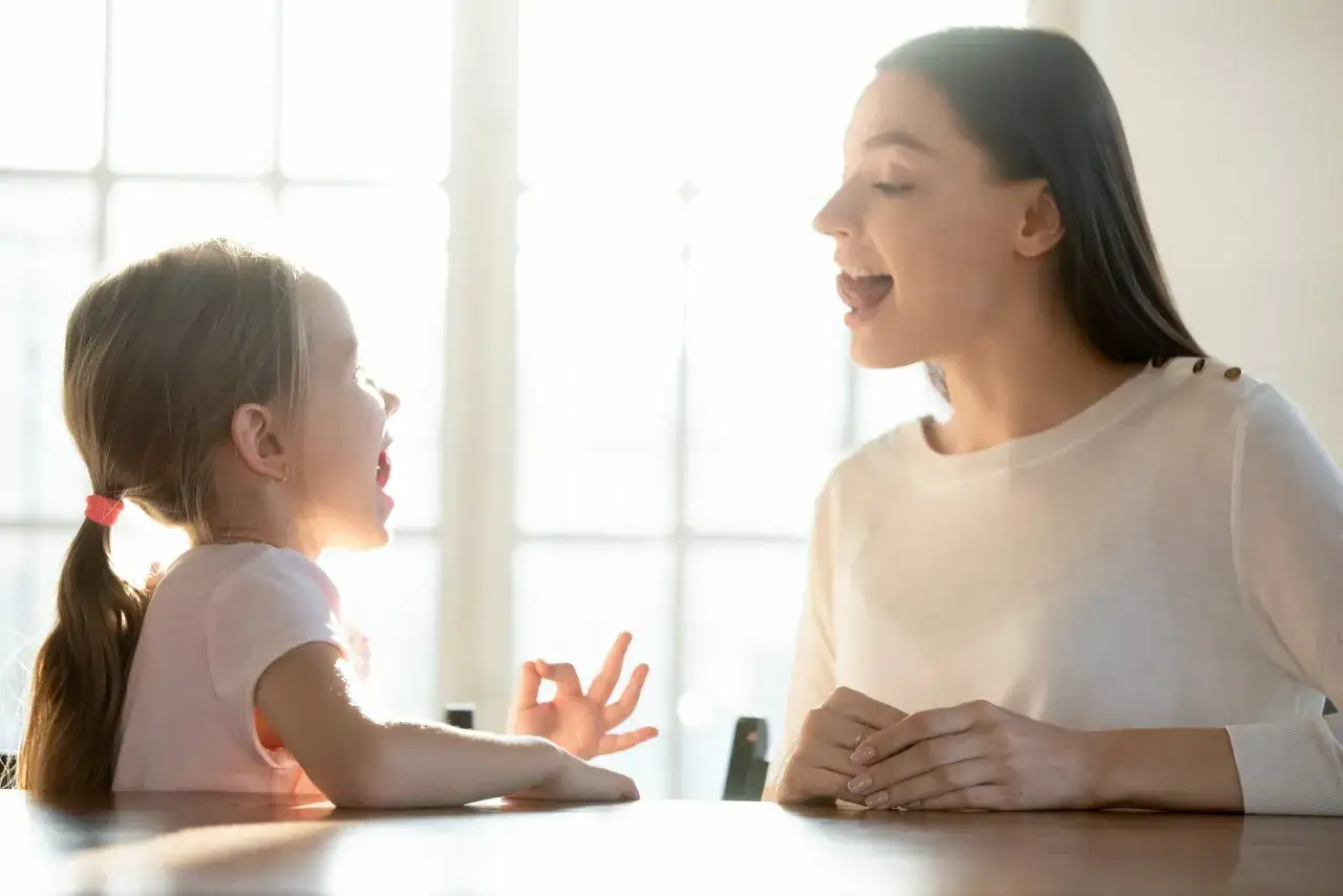 Uśmiechnięta mama i dziecko ćwiczą wymowę. Dziecko mruczy podczas zabawy, naśladując mamę.