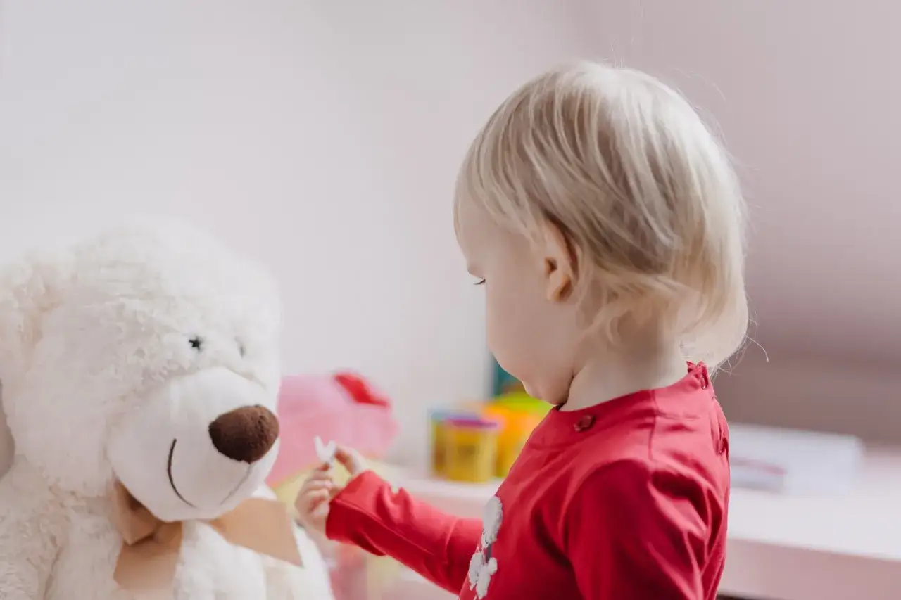 Dziecko w czerwonej bluzce podaje motylka wielkiemu białemu misiowi. Czasem sztywność zachowania i myślenia objawia się w zabawie.
