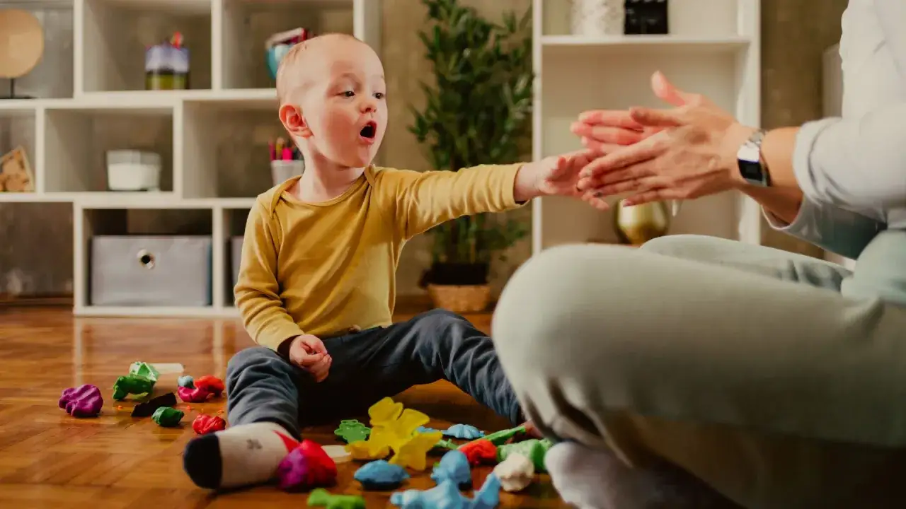 Chłopiec z wrażliwością sensoryczną bawi się plasteliną, a mama klaszcze. Przykłady interakcji.