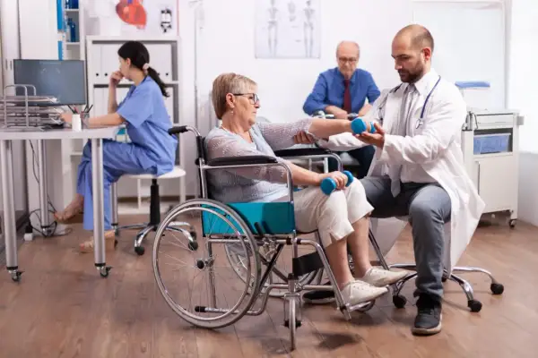 Rehabilitacja po udarze krwotocznym. Lekarz pomaga pacjentce w wózku inwalidzkim ćwiczyć z hantlami, poprawiając rokowania.