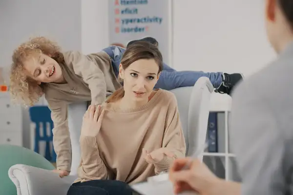 Matka rozmawia z terapeutą o różnych rodzajach ADHD, podczas gdy jej syn z nadpobudliwością bawi się za jej plecami.